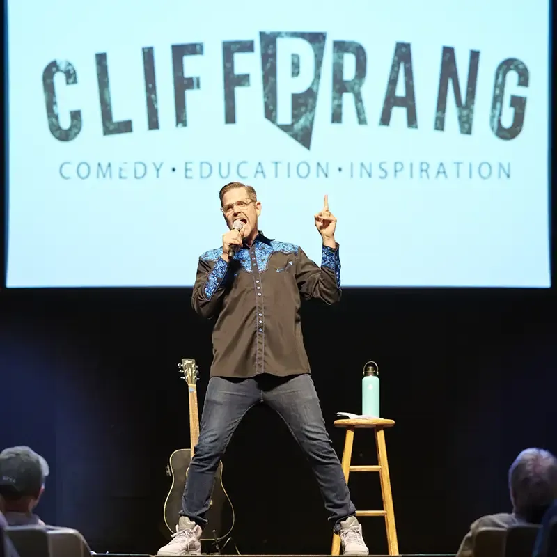 Cliff in front of screen pointing upwards with mic in hand